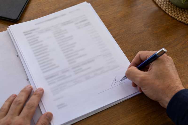 Main signant la dernière page d'un inventaire agrafé sur une table